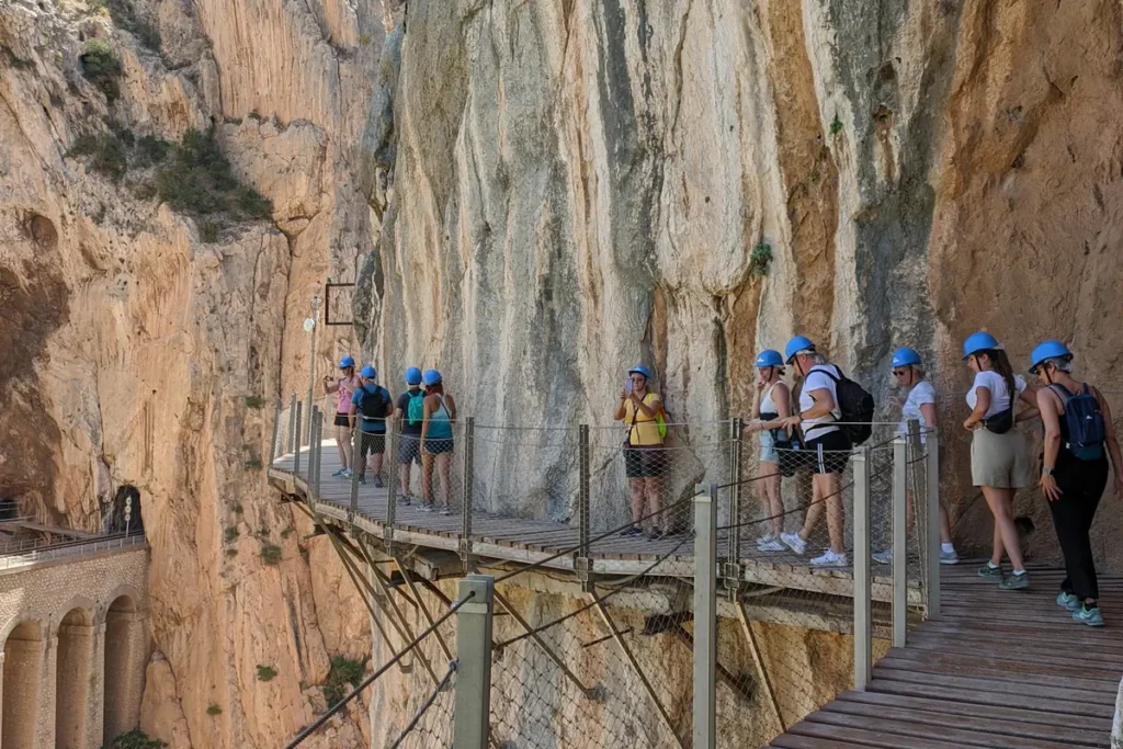 Walkers in helmets on the Caminito del Rey boardwalk between limestone walls