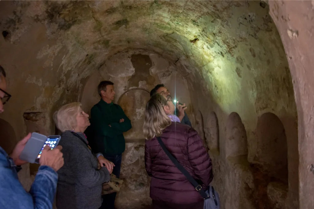 Visitors inside a vaulted underground tomb chamber in Carmona