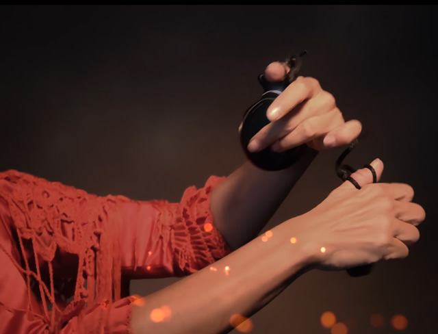 A dancer holding castanets, hands lit against a red background