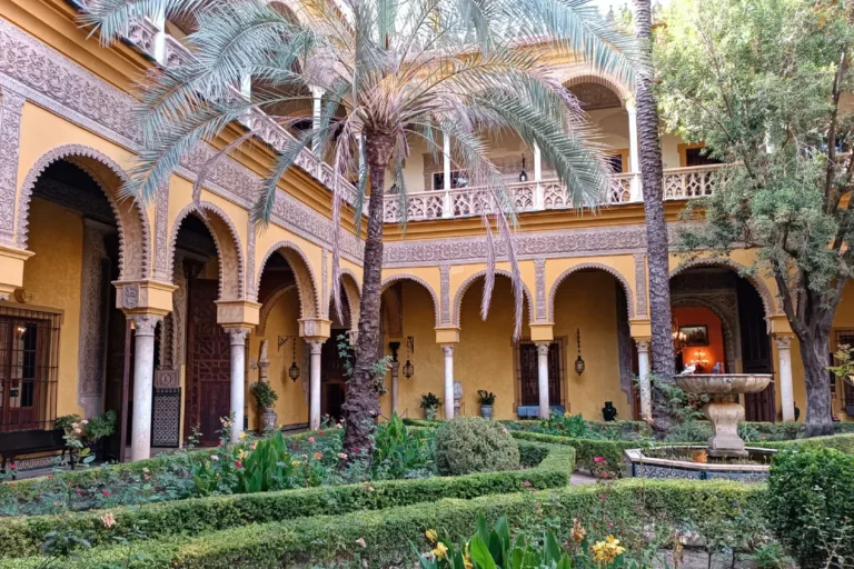 The arcaded courtyard of the Palacio de las Duenas in Seville, with palms and clipped hedges