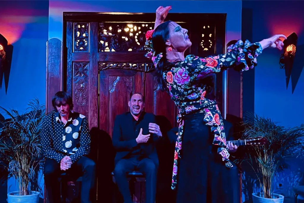 A flamenco dancer mid-move with the musicians behind her at a tablao in Triana