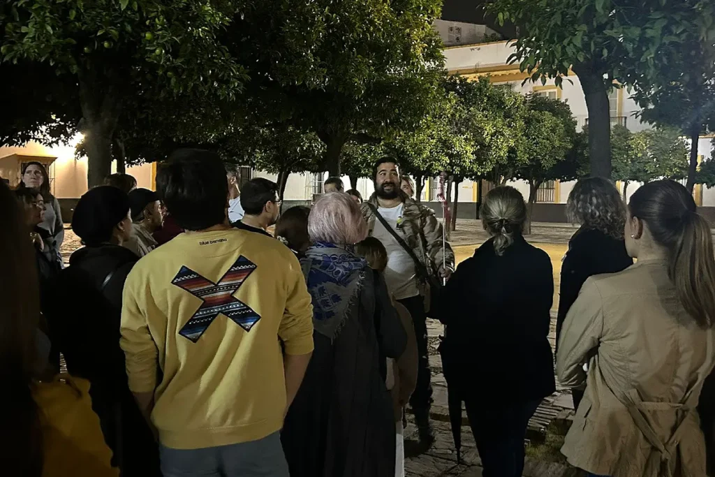 A walking tour group listening to their guide in the streets of Seville after dark