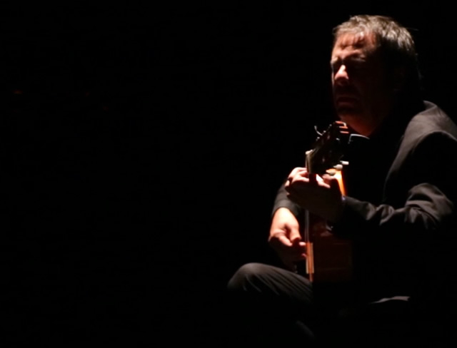 A flamenco guitarist playing alone on a darkened stage in Seville