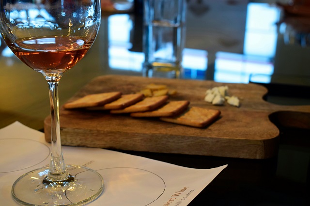 A glass of wine beside a wooden board with bread and cheese