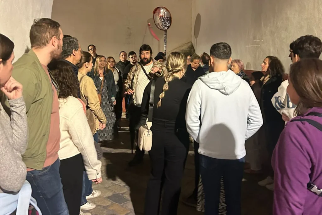 A guide telling stories to a group in a narrow Seville street at night