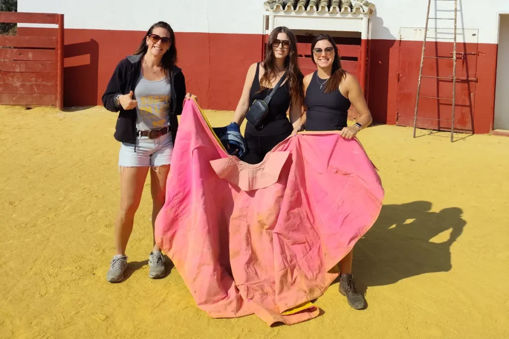 Visitors holding a bullfighting cape in the small testing ring of the ranch