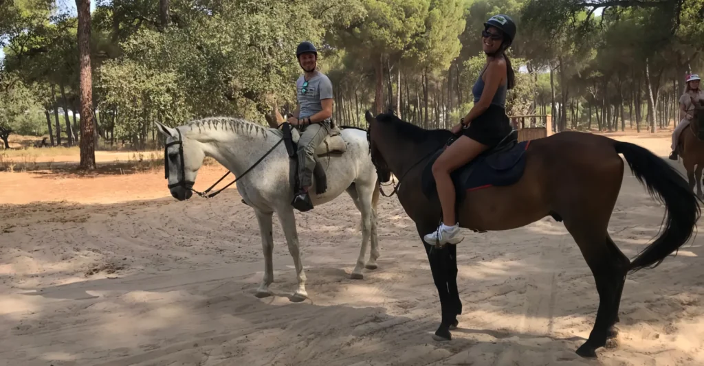 Two riders on horseback among umbrella pines in the countryside near Seville