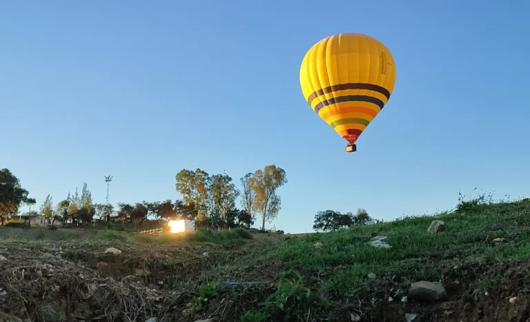 A yellow hot air balloon flying low over the countryside near Seville