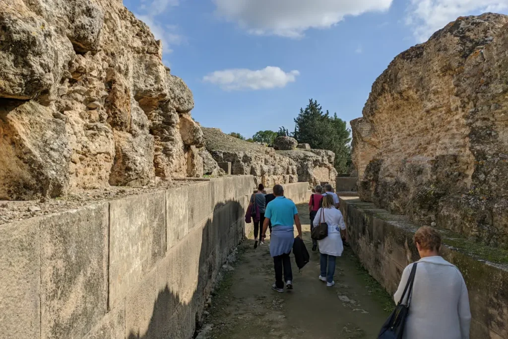 Visitors walking a paved Roman street between the walls of Italica