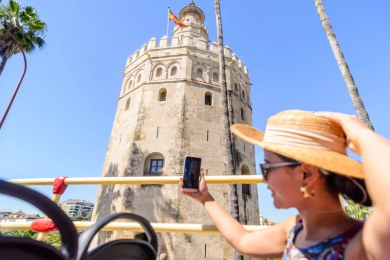A passenger on the top deck of an open-top bus photographing the Torre del Oro