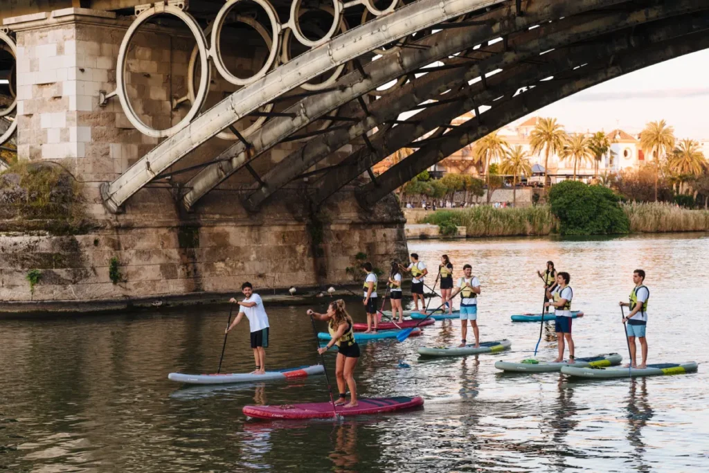 A paddle surf group passing under the ironwork of the Triana bridge