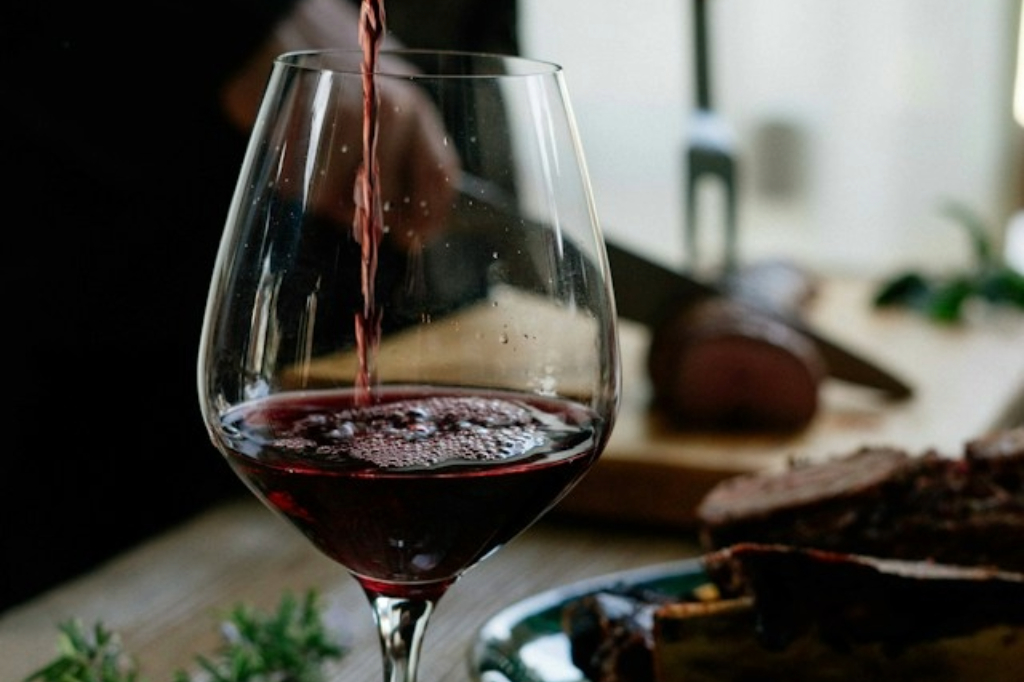 Red wine being poured into a glass beside a board of food