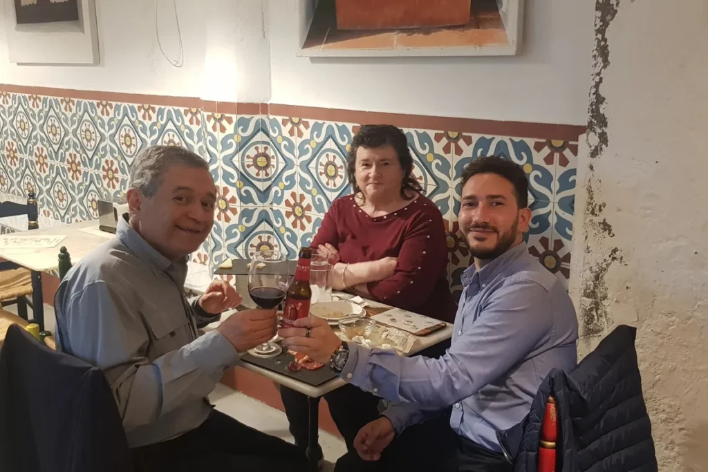 Three people raising their glasses at a tiled table in a Seville bar