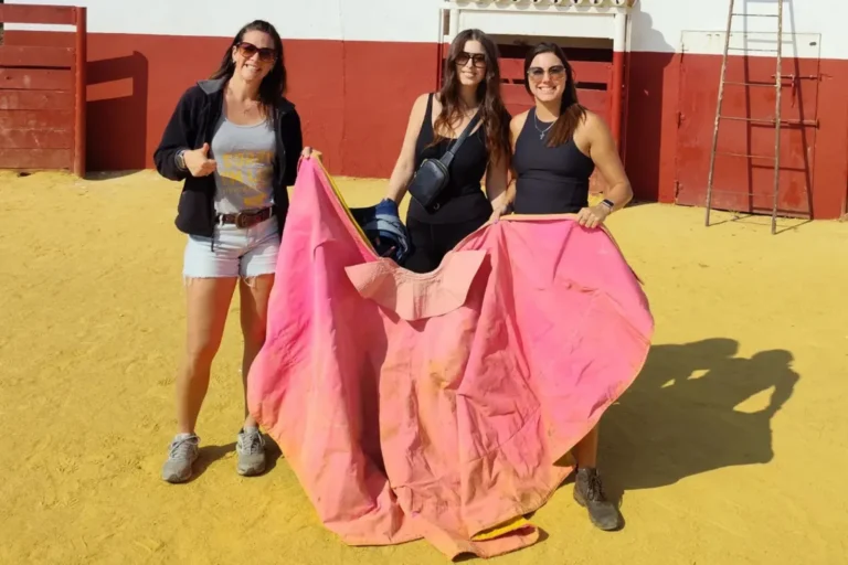 Three travelers holding a pink cape in an Andalusian bullring