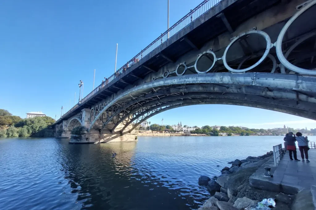 Looking up at the ironwork of the Triana bridge from the riverbank in Seville