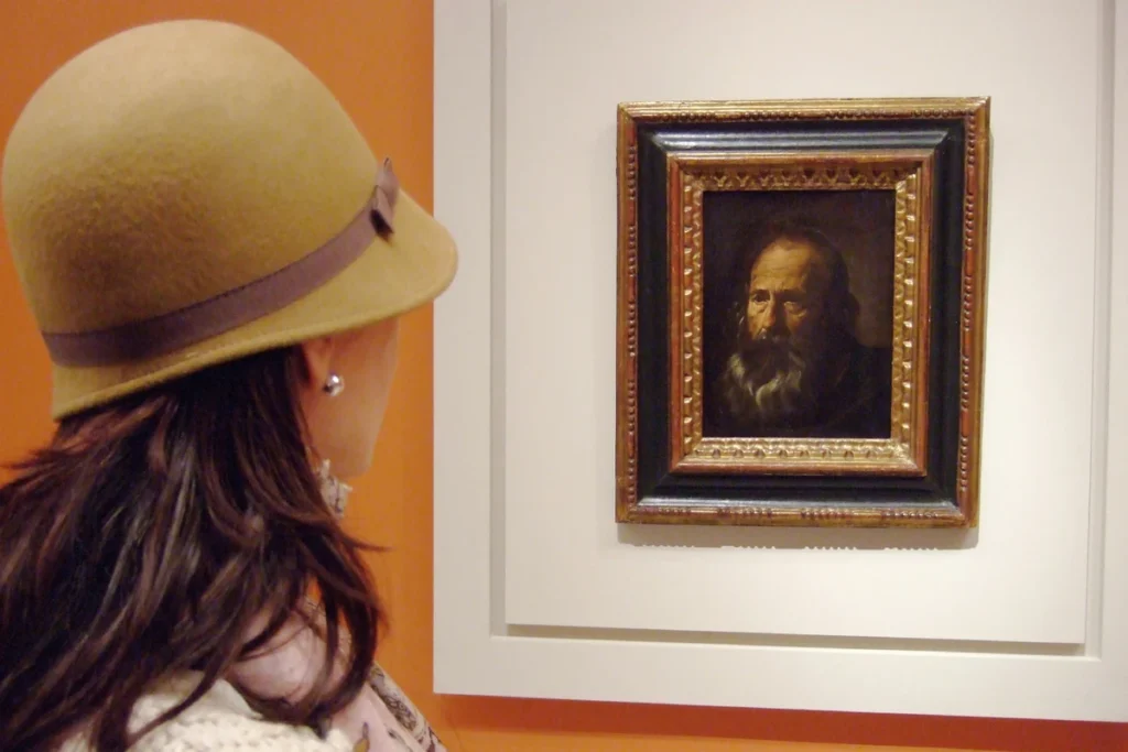 A visitor looking closely at a small framed portrait in the Museum of Fine Arts of Seville