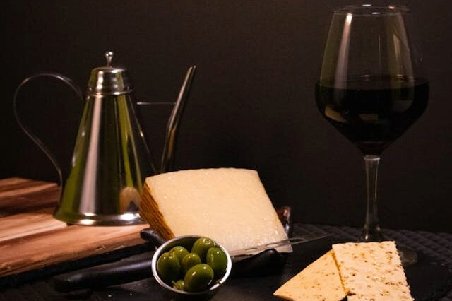 A glass of red wine with cheese, olives and crackers